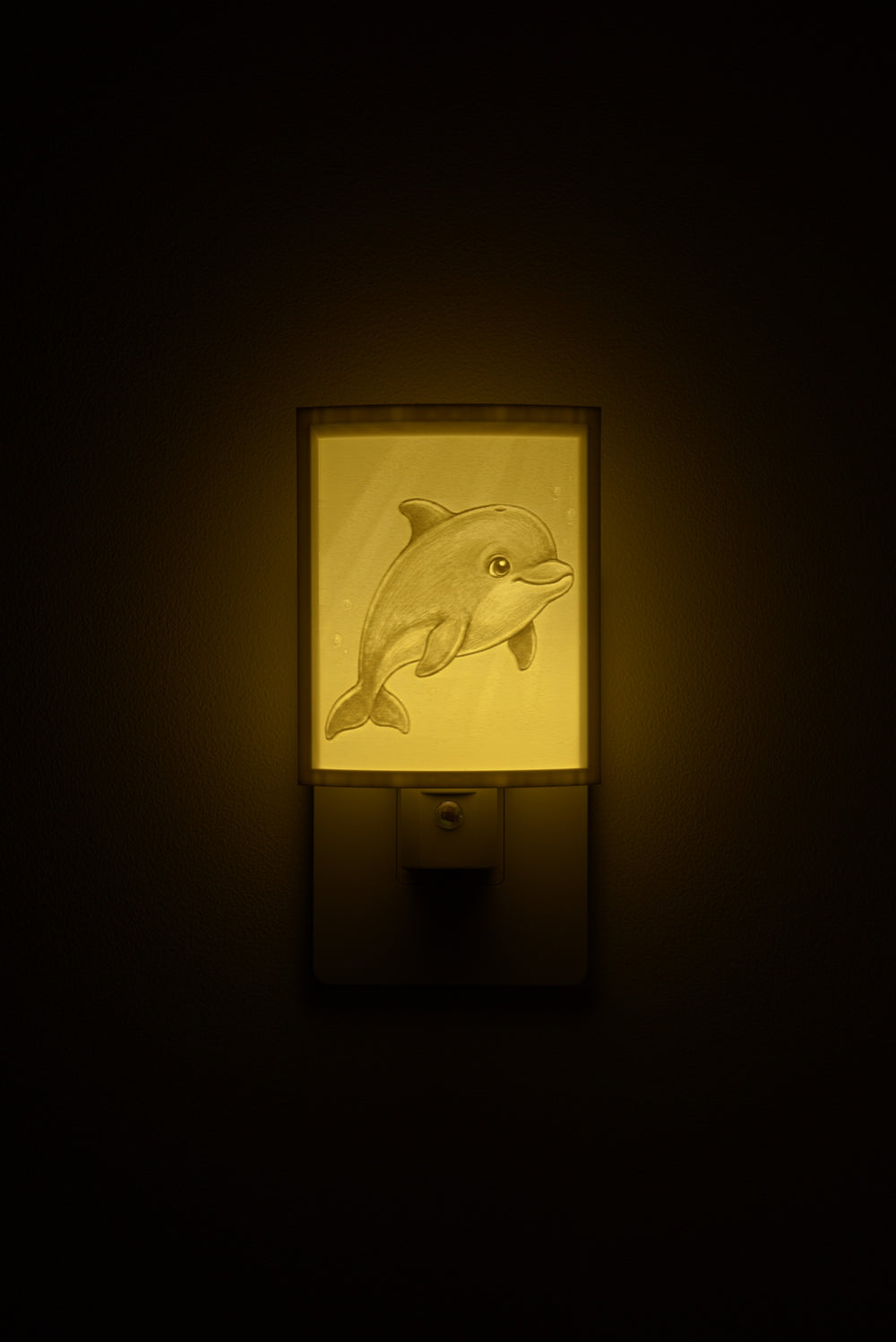 Dolphin night light glowing against a dark wall, plugged into an outlet