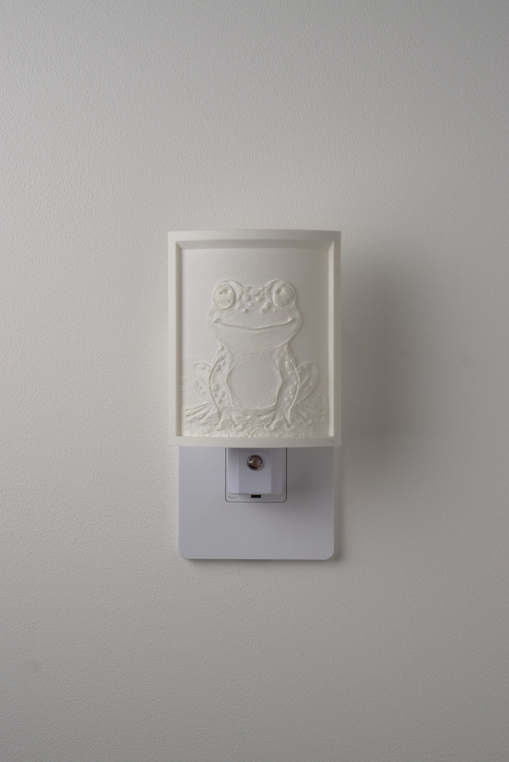 Frog night light switched off — a soft ivory panel by day