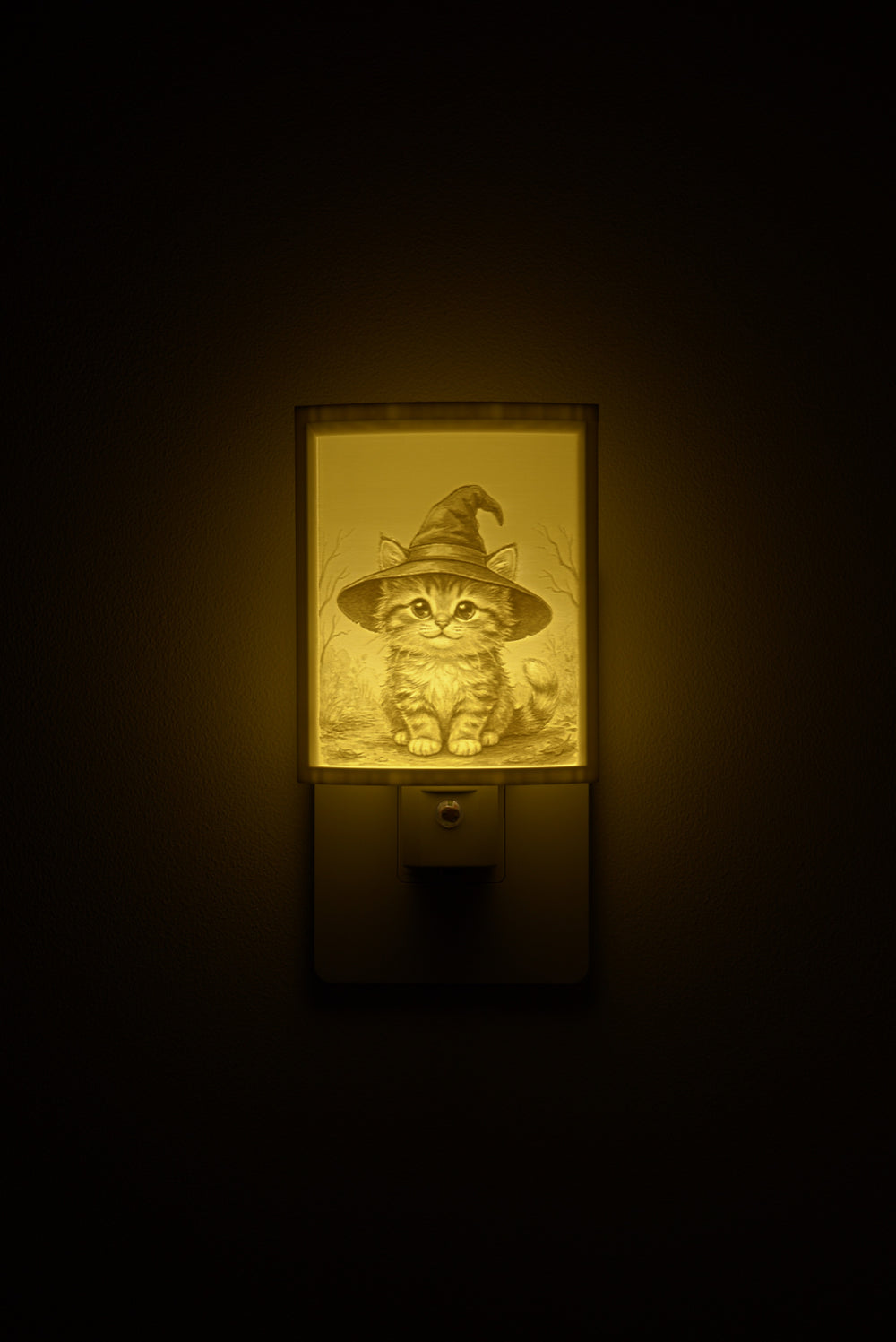 Kitten in a Witch Hat night light glowing against a dark wall, plugged into an outlet