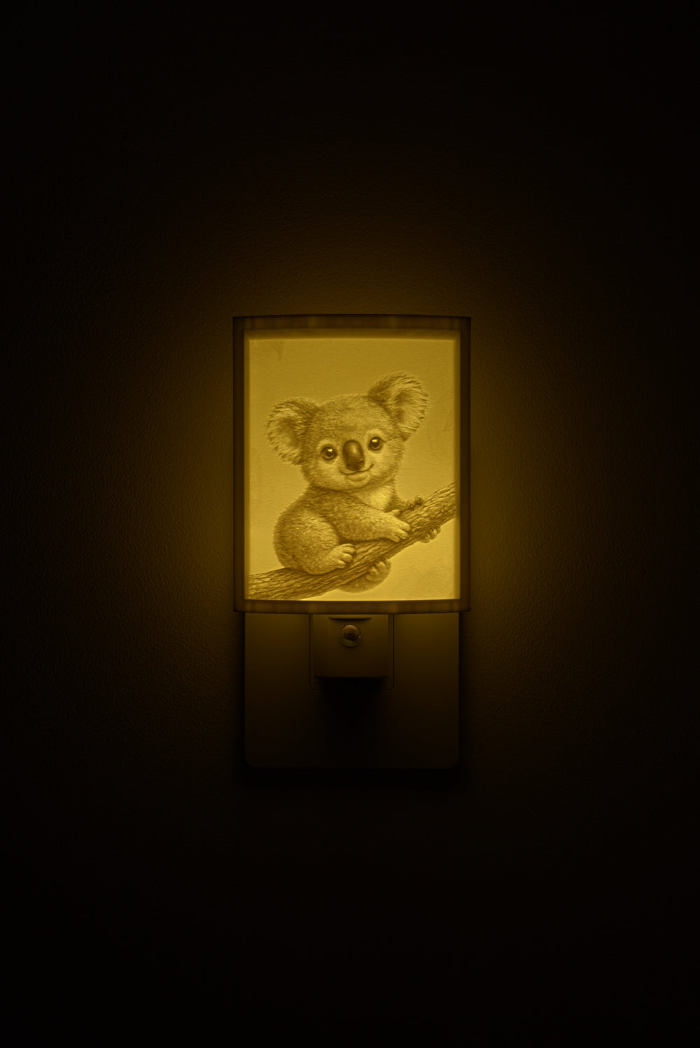 Koala night light glowing against a dark wall, plugged into an outlet