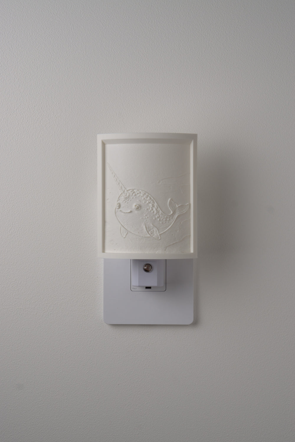 Narwhal night light switched off — a soft ivory panel by day