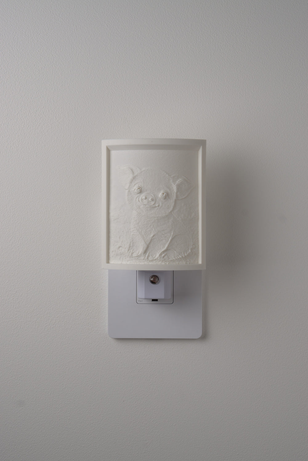 Pig night light switched off — a soft ivory panel by day