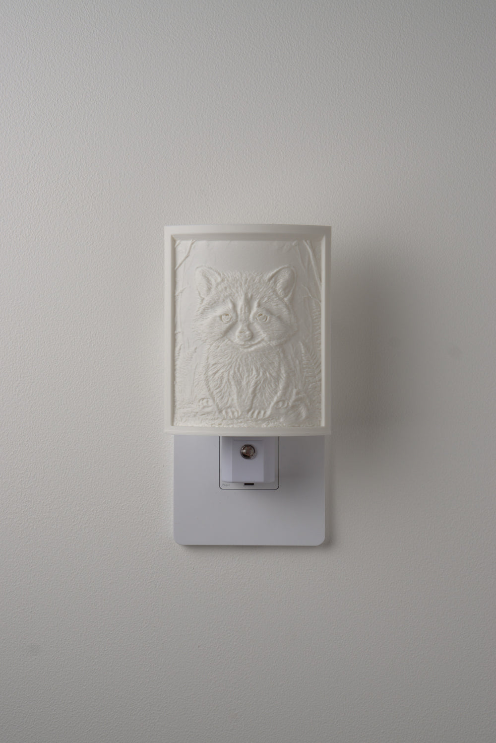 Raccoon night light switched off — a soft ivory panel by day