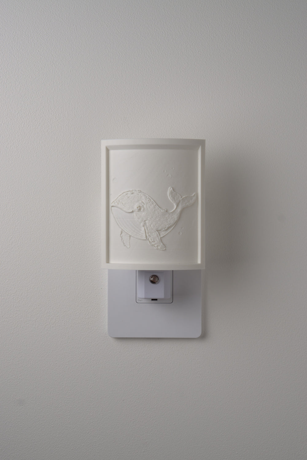 Whale night light switched off — a soft ivory panel by day