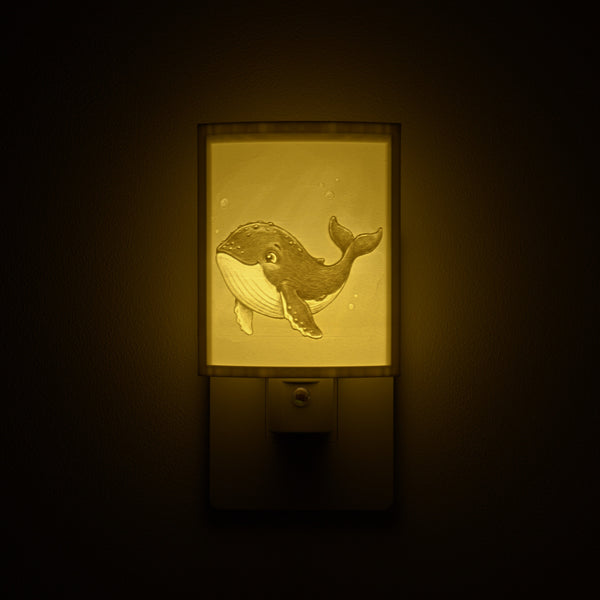 Whale night light glowing against a dark wall, plugged into an outlet