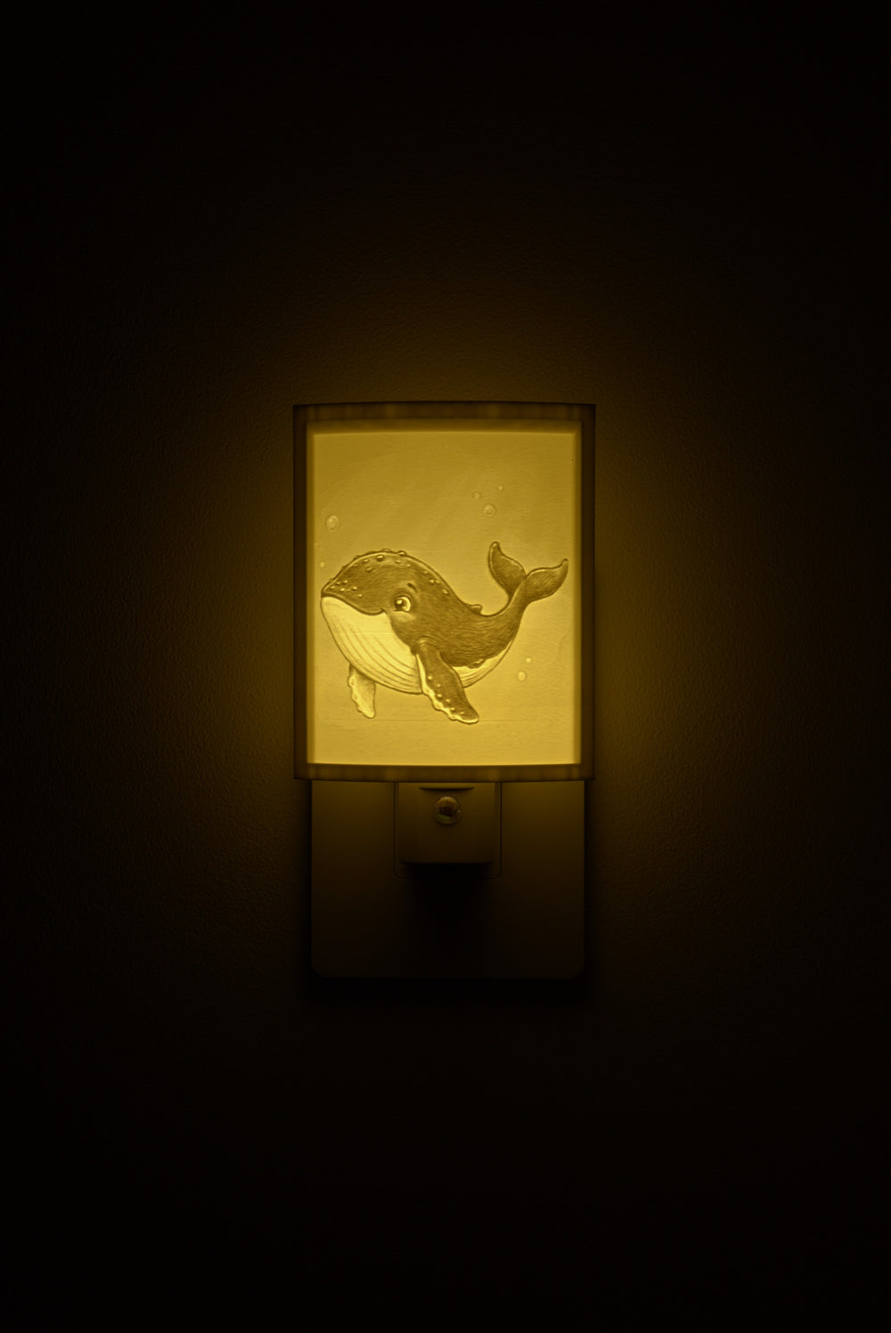Whale night light glowing against a dark wall, plugged into an outlet