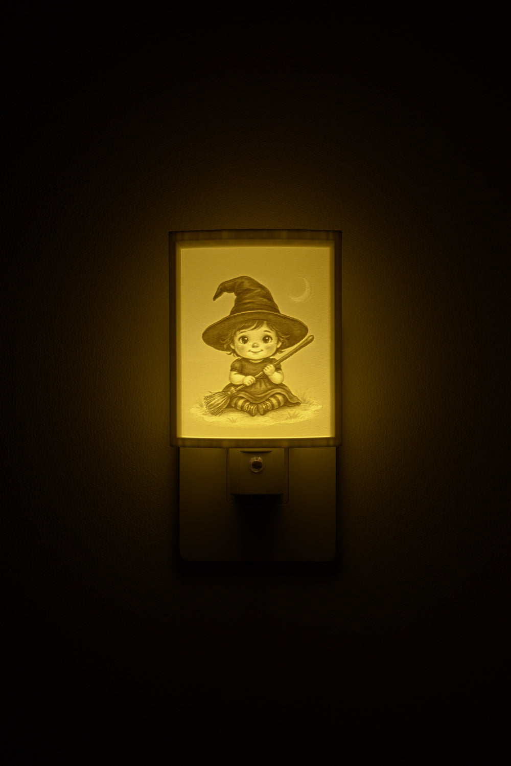 Little Witch night light glowing against a dark wall, plugged into an outlet